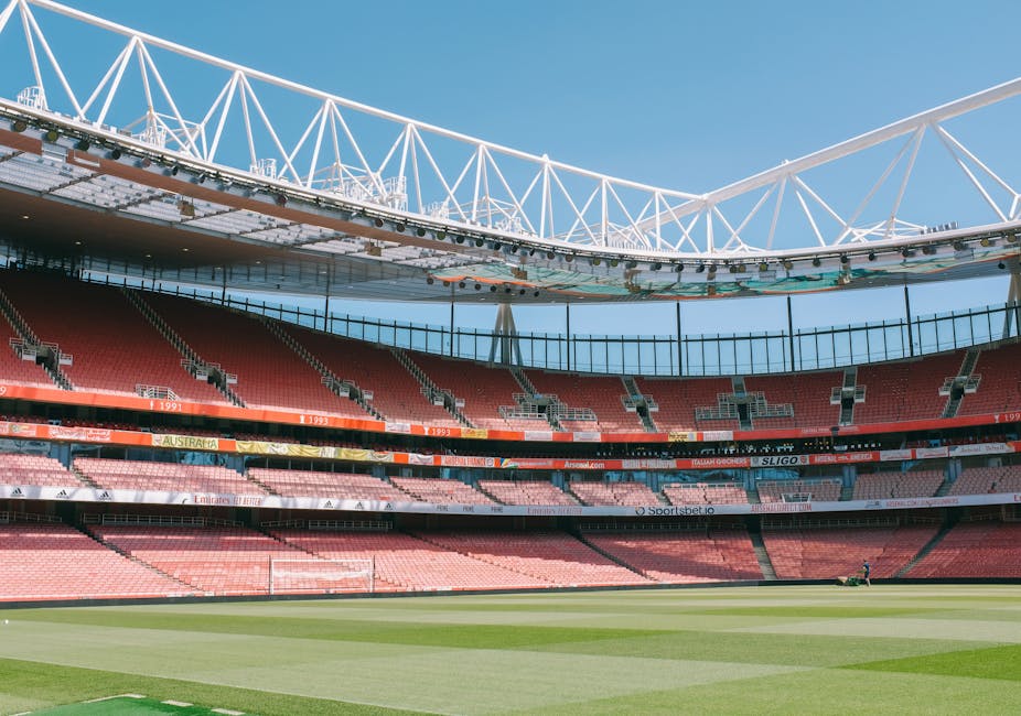 A panoramic view of Wembley Stadium's interior during a sporting event, showcasing the well-maintained grass pitch with visible white boundary lines and goalposts at each end. The surrounding seating 